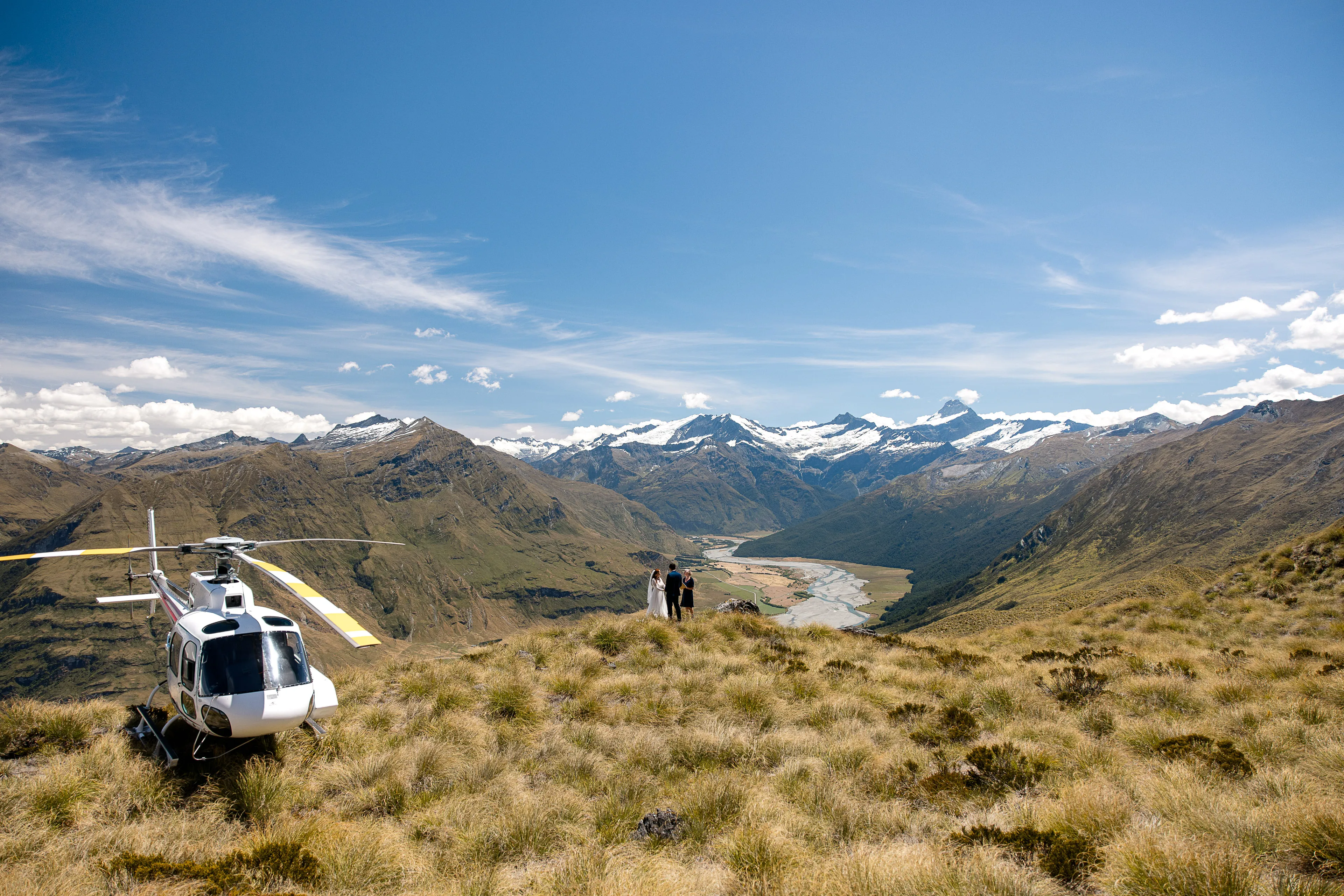 A helicopter beside a bride, groom and celebrant on a tussock ridge at Alta Tarns above the Matukituki Valley