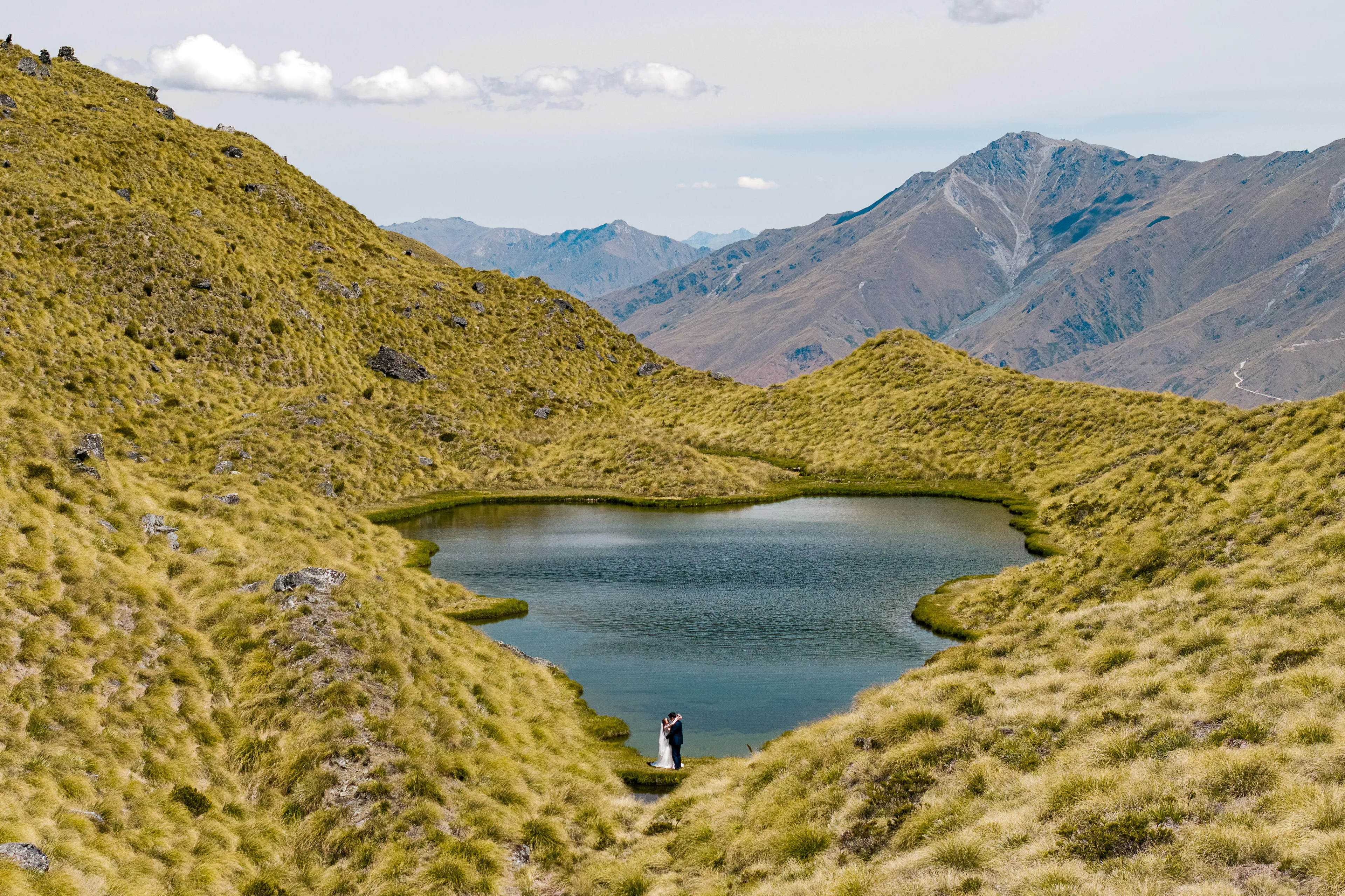 A couple embracing beside a heart-shaped alpine tarn at Alta Tarns above Wānaka