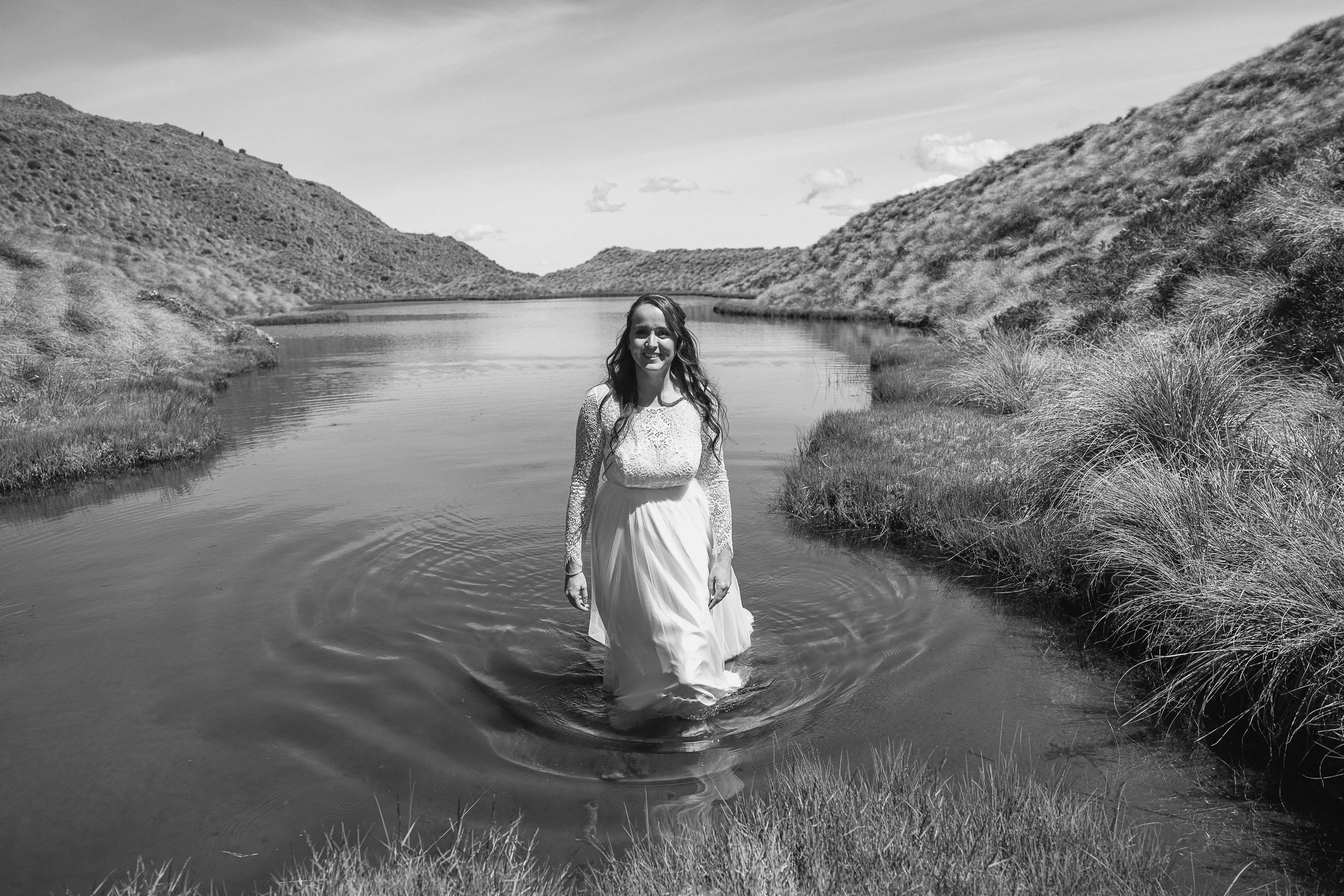 A black-and-white portrait of a bride standing in a still alpine tarn at Alta Tarns