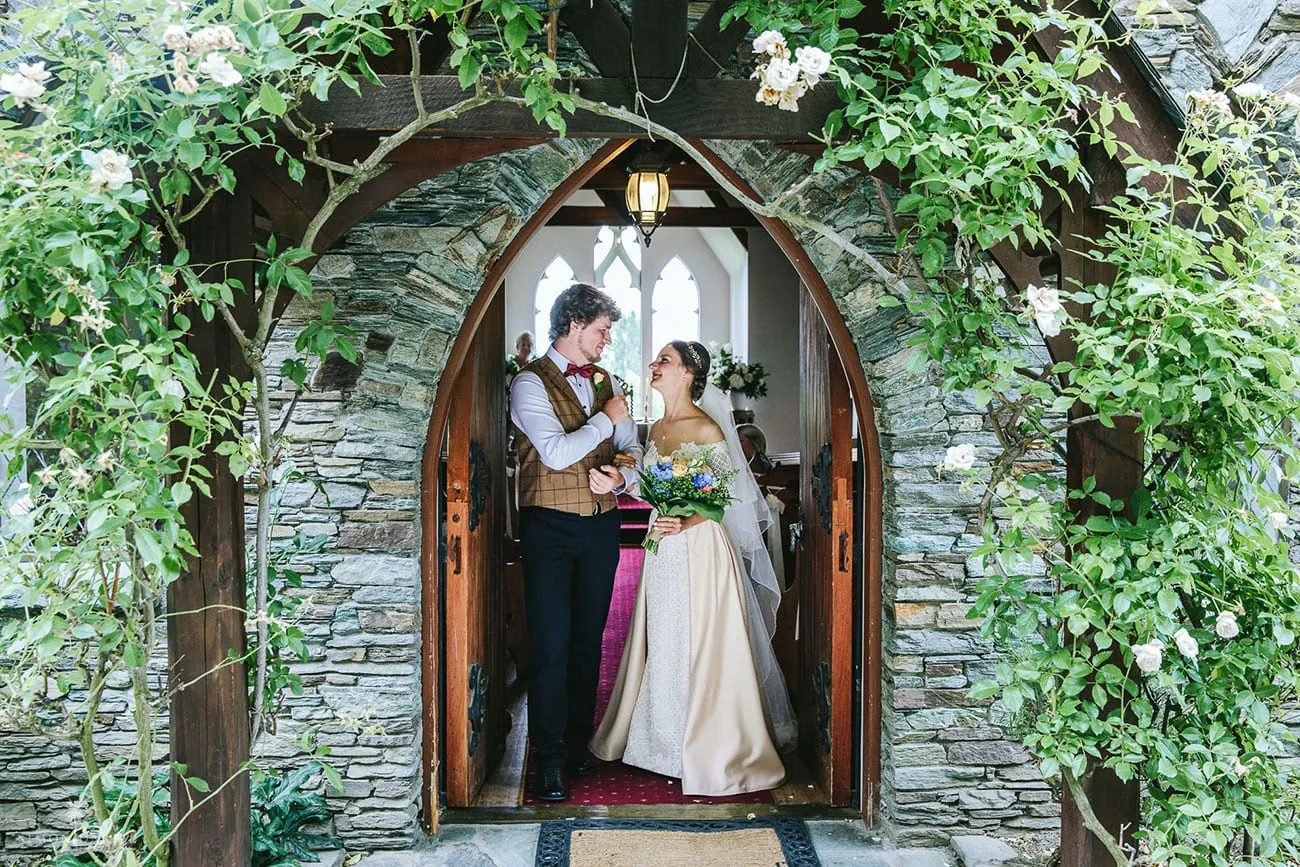 A bride and groom in the rose-covered stone doorway of Chapel by the Lake