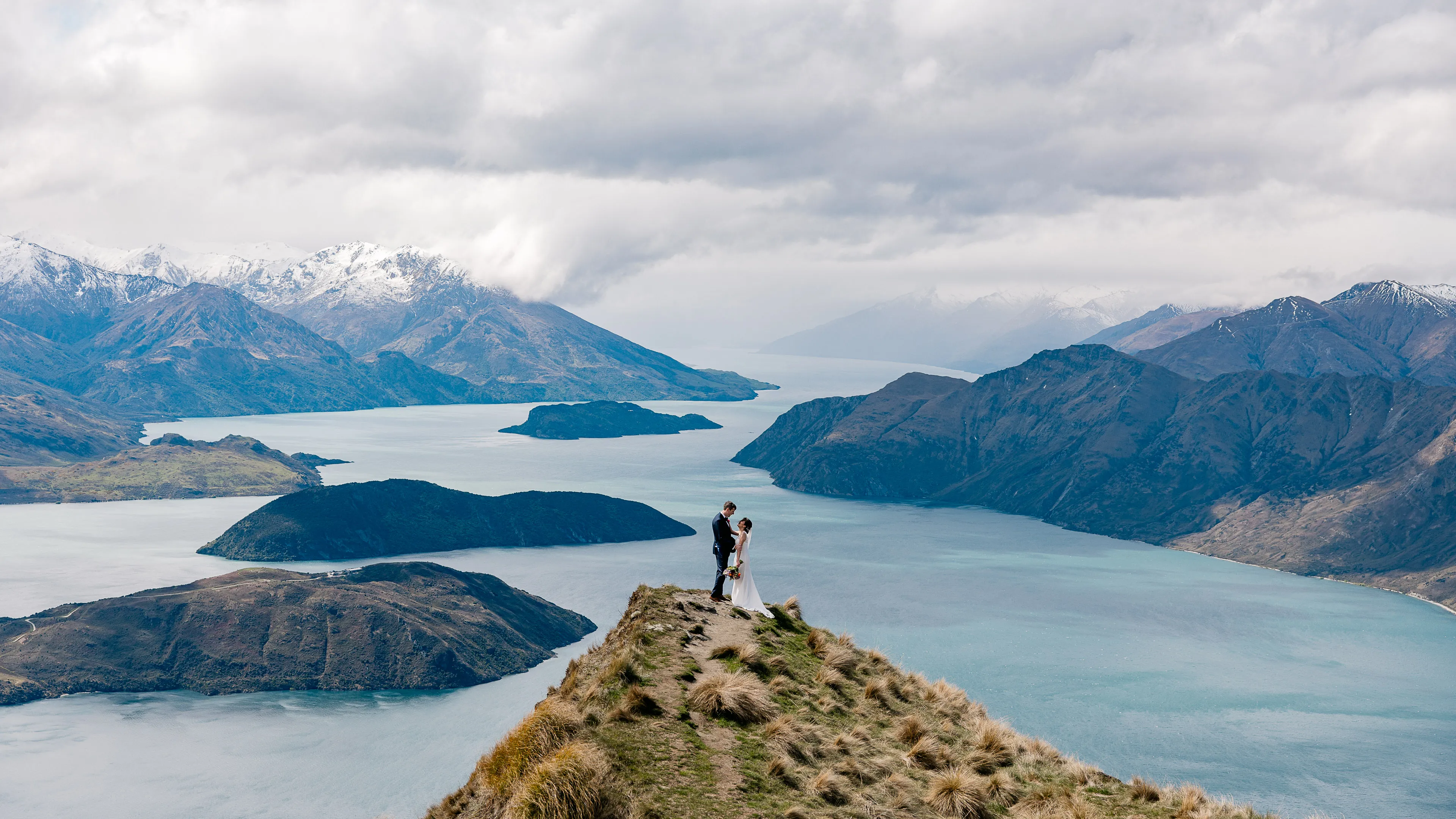 A couple standing together on Coromandel Peak, high above Lake Wānaka and its islands
