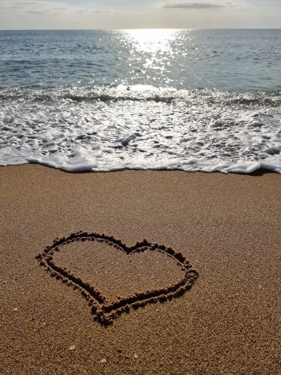 Heart drawn in the sand at the water's edge as a wave rolls in