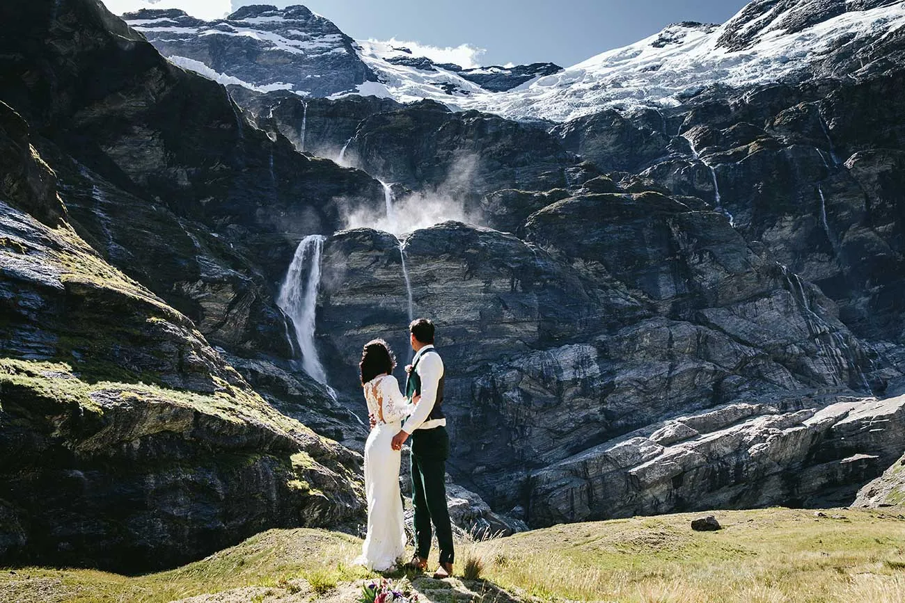 A couple watching a waterfall cascade down the cliffs of Earnslaw Burn