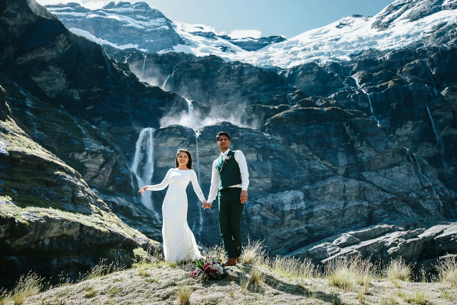A bride and groom at Earnslaw Burn with cascading waterfalls and a hanging glacier behind them