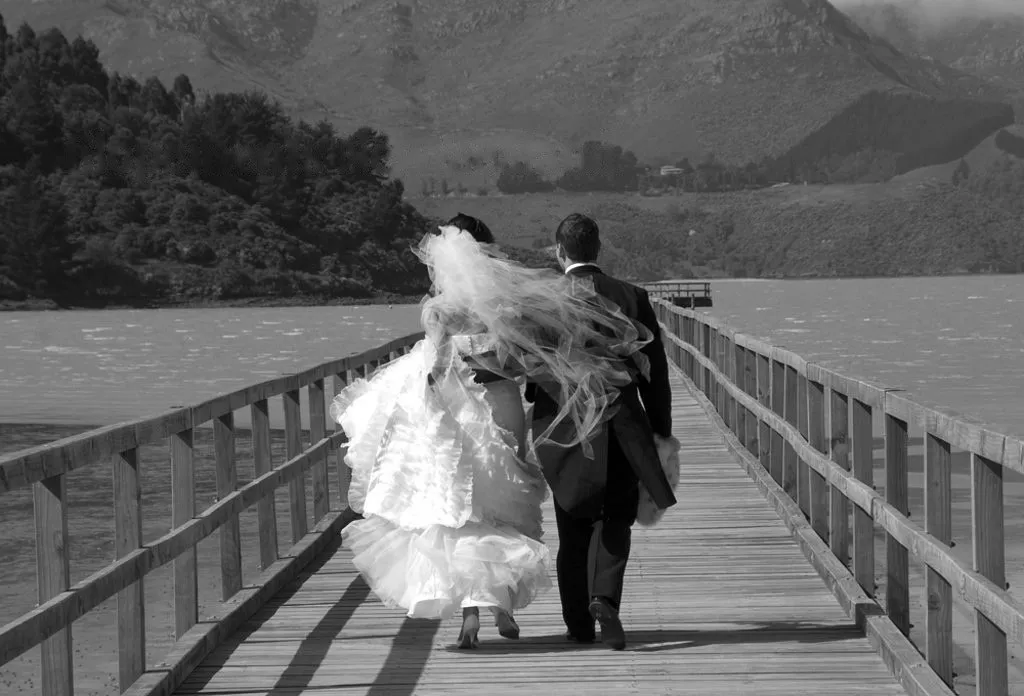 Bride and groom walking hand in hand along a lake jetty in New Zealand, black and white