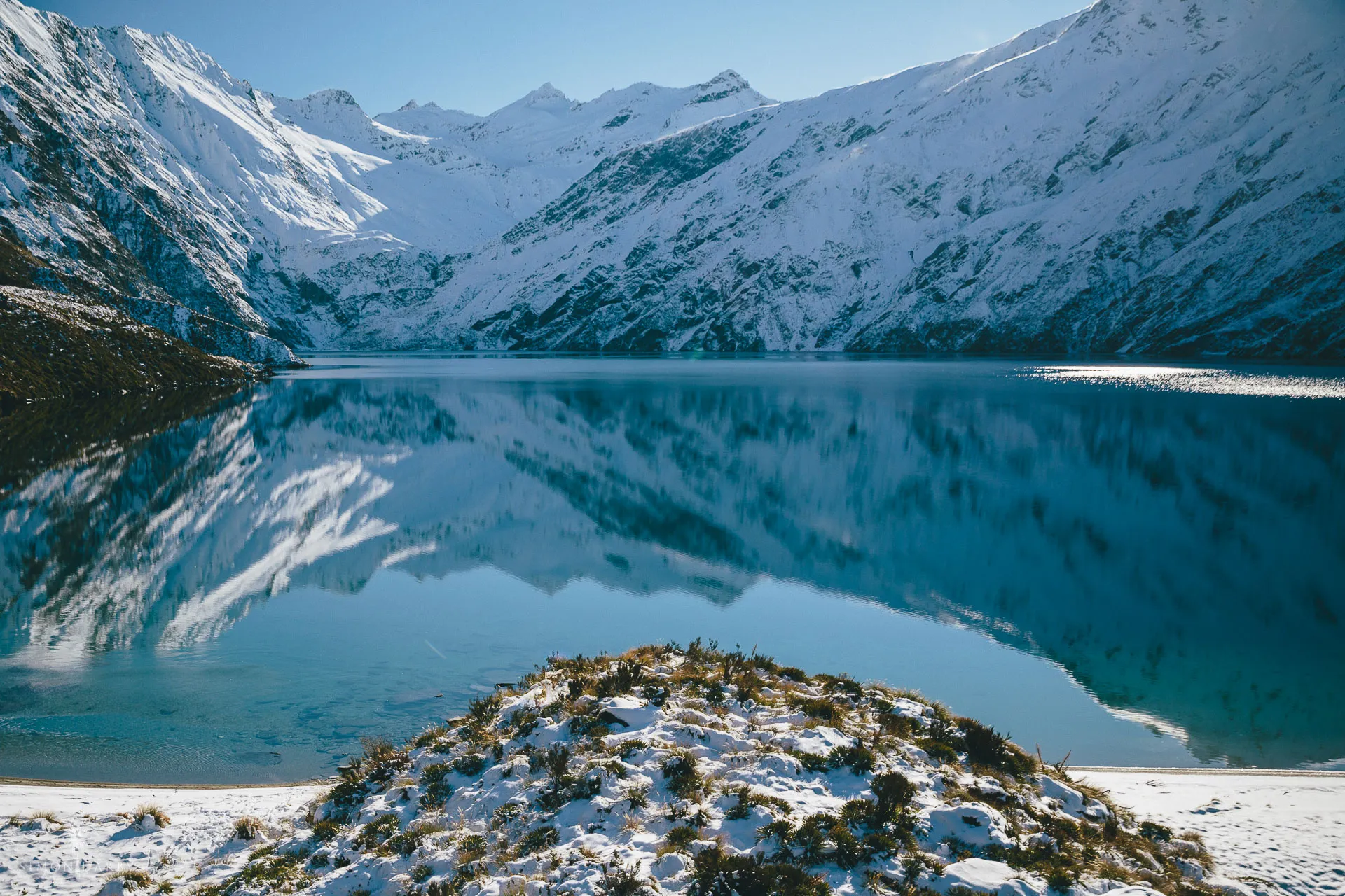 Snow-covered mountains mirrored in the calm waters of remote Lake Lochnagar