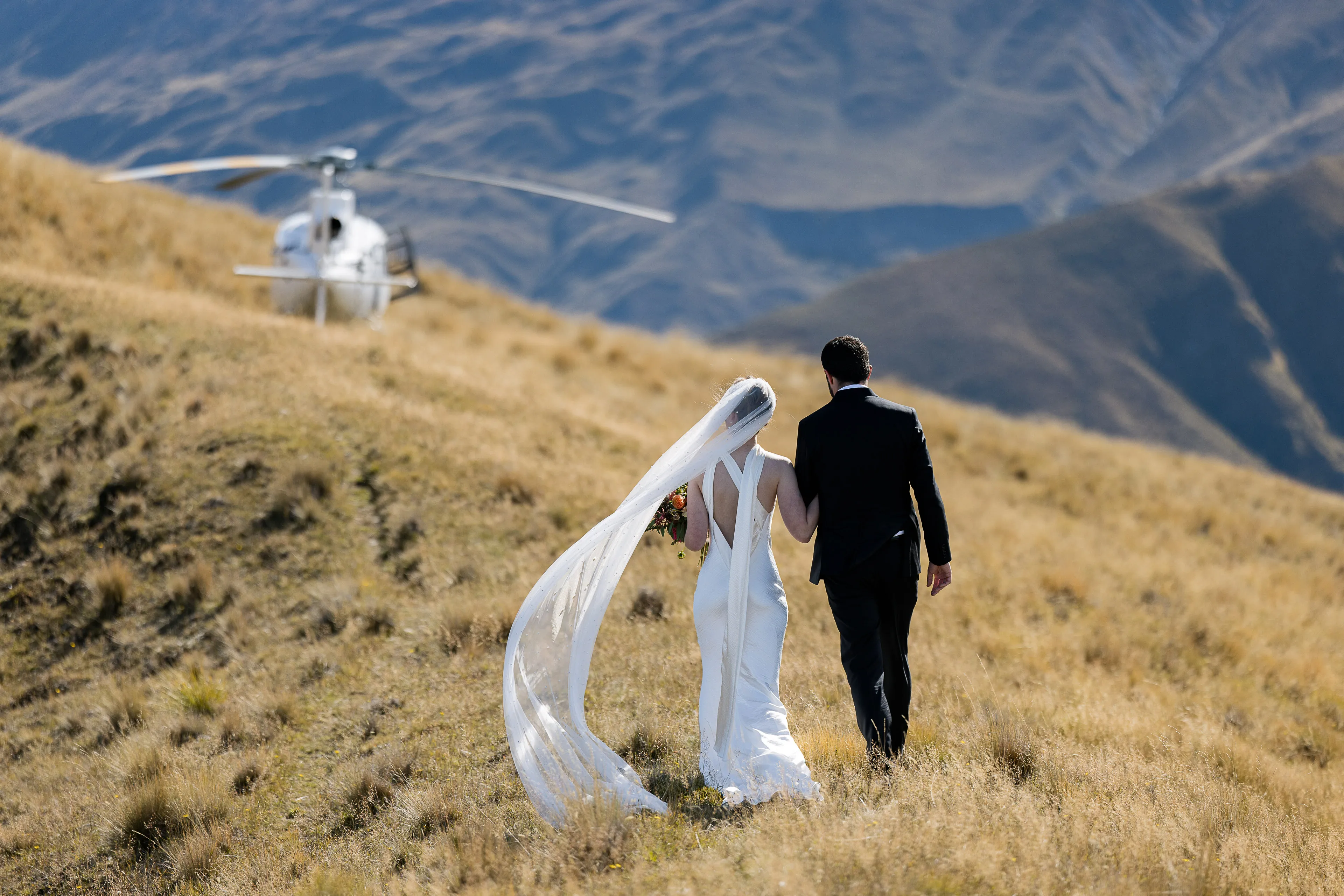 A bride and groom walking to the helicopter on Lookout Hill, the bride's veil streaming in the wind