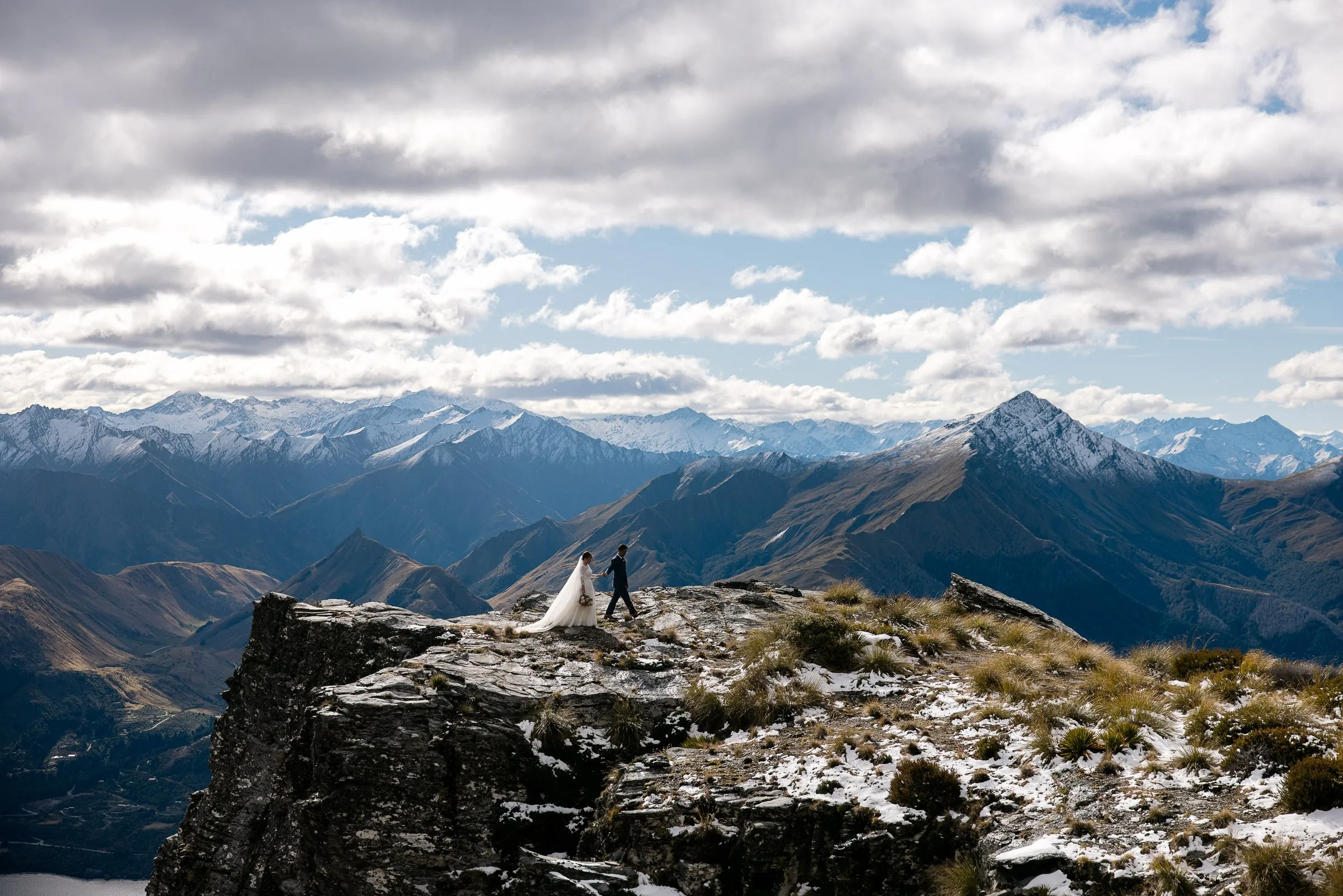 The Ledge, Cecil Peak Bride and groom walking along The Ledge on Cecil Peak with the Queenstown mountains behind