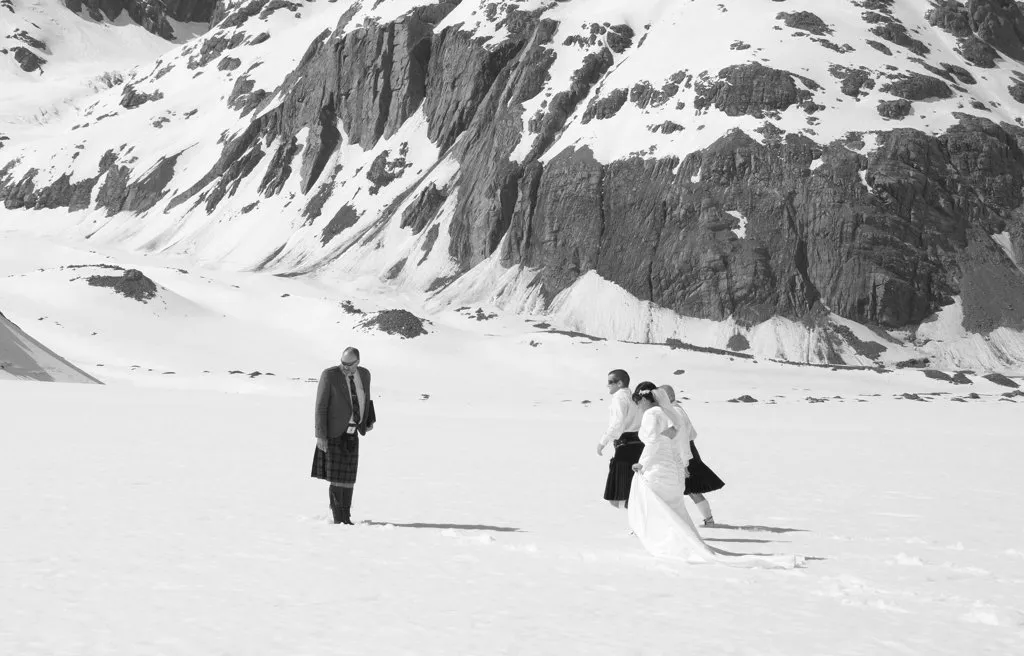 A couple and their celebrant on the snow of Richardson Glacier, beneath towering alpine cliffs