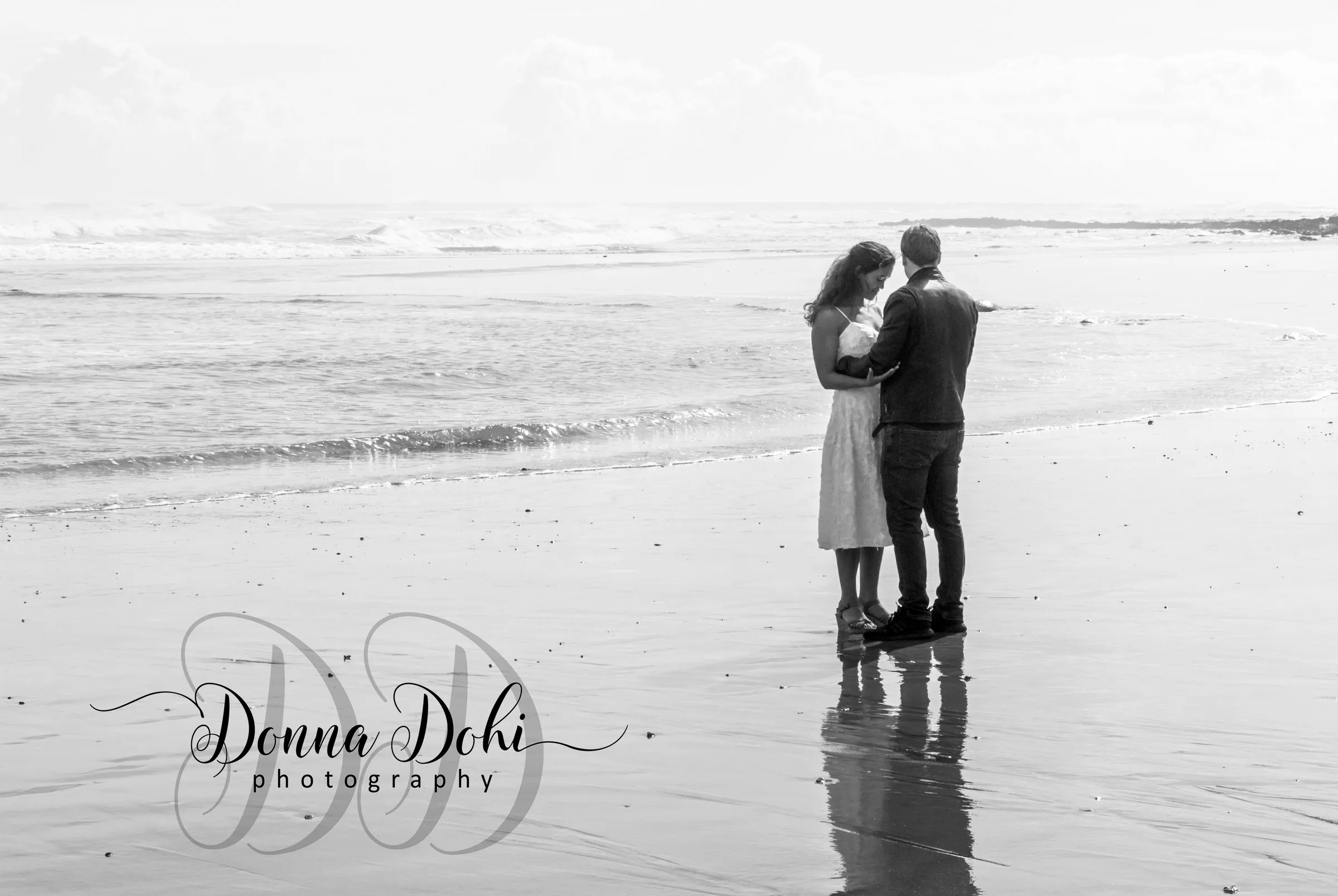 Couple standing together at the water's edge on a New Zealand beach, black and white