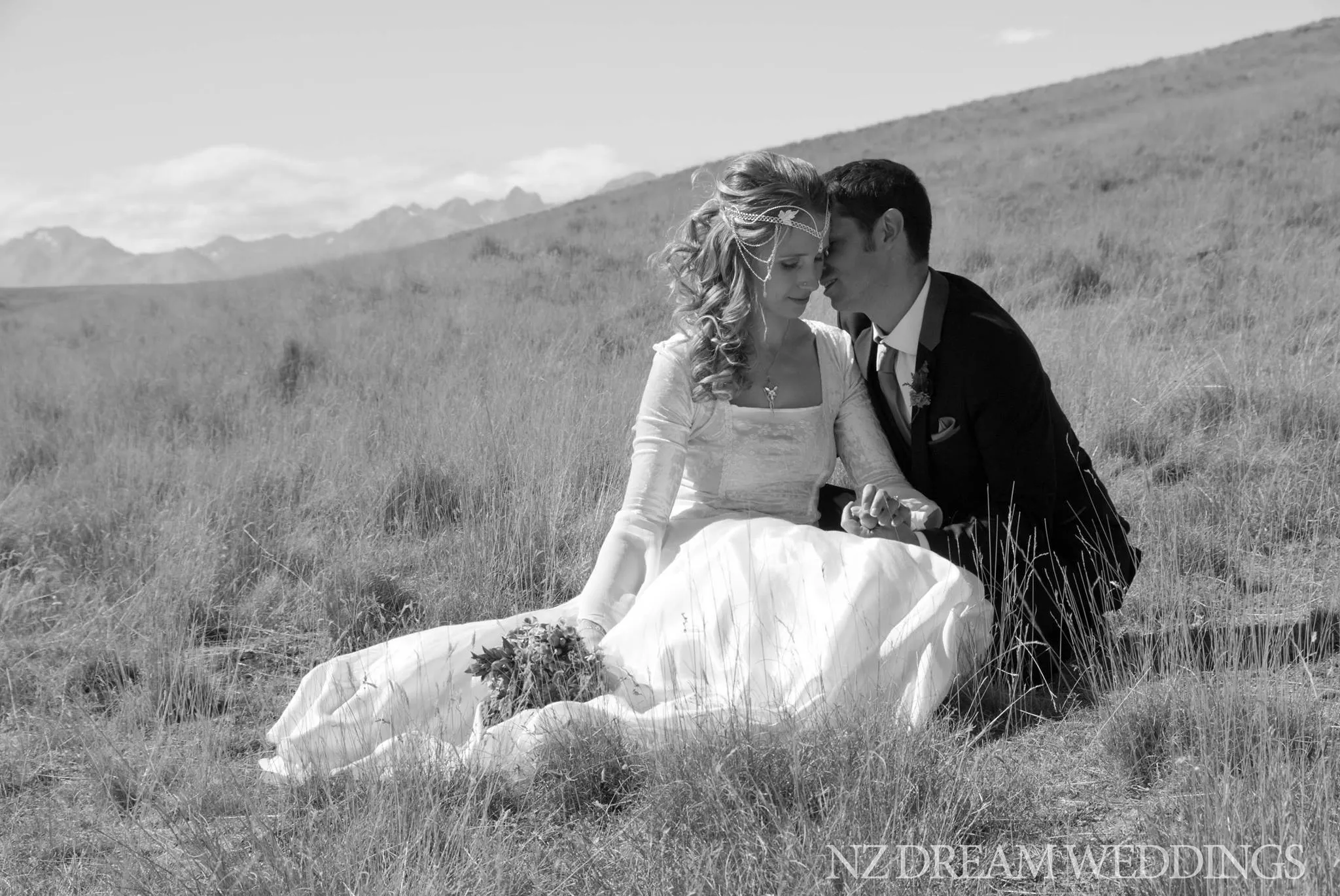 Bride and groom sitting close together in alpine grassland, black and white