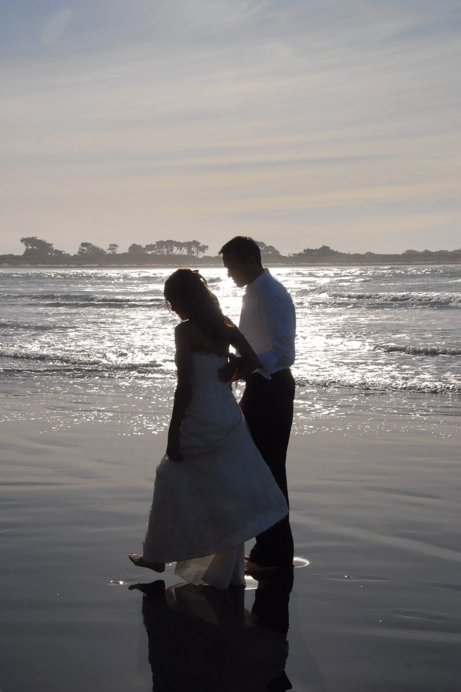 Newly married couple walking through the shallows on a New Zealand beach at sunset