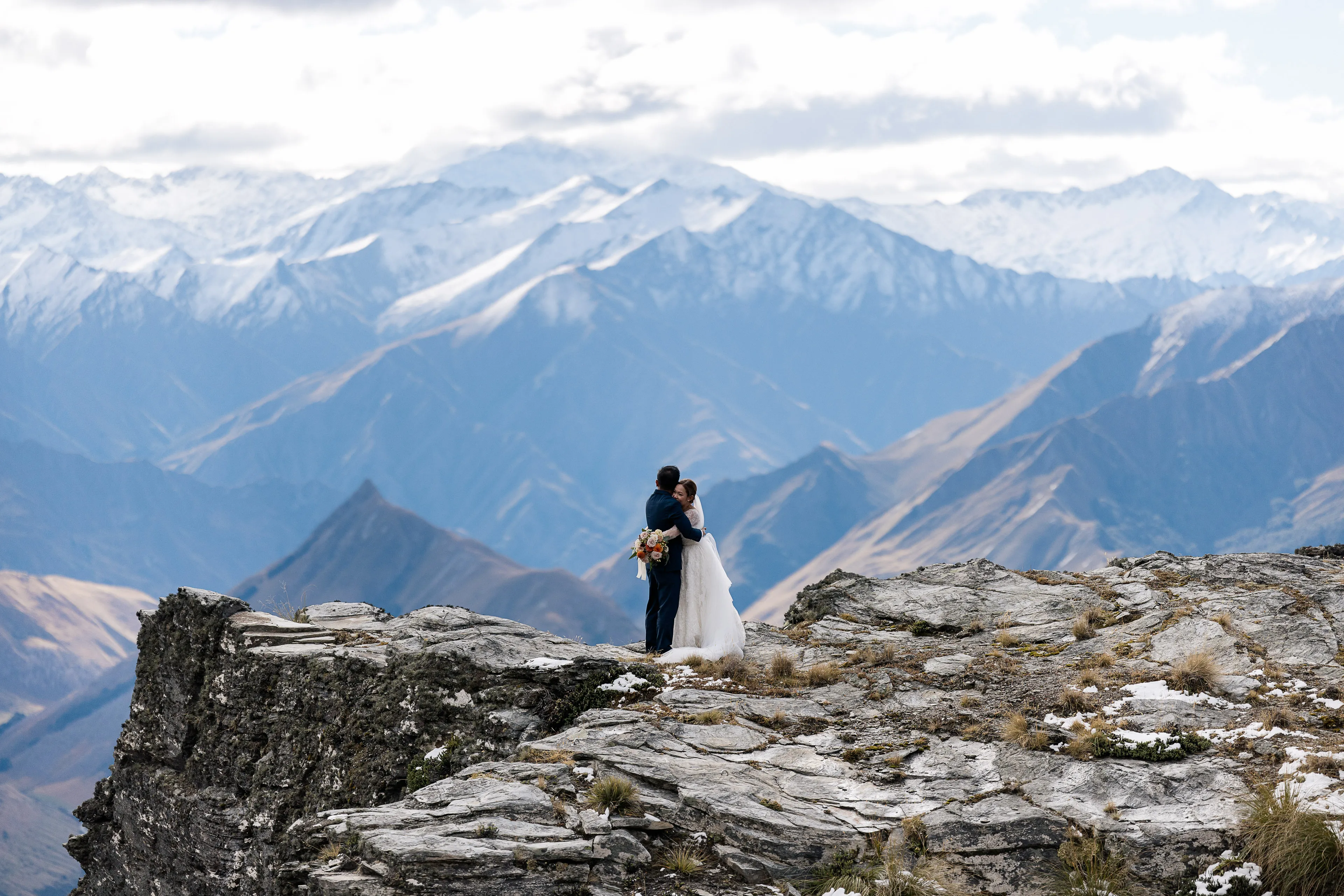 A couple embracing on The Ledge at Cecil Peak with snow-capped mountains behind them