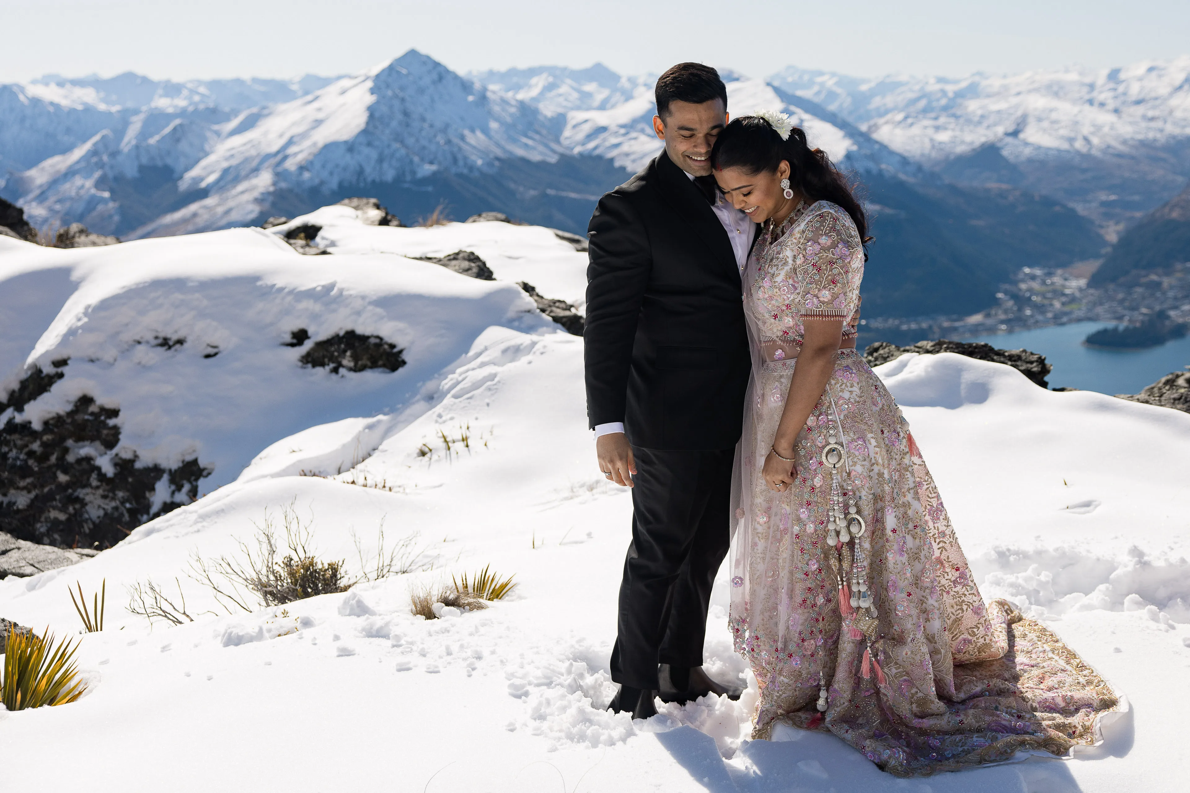 A couple embracing in the snow on The Ledge at Cecil Peak, Lake Wakatipu and Queenstown far below