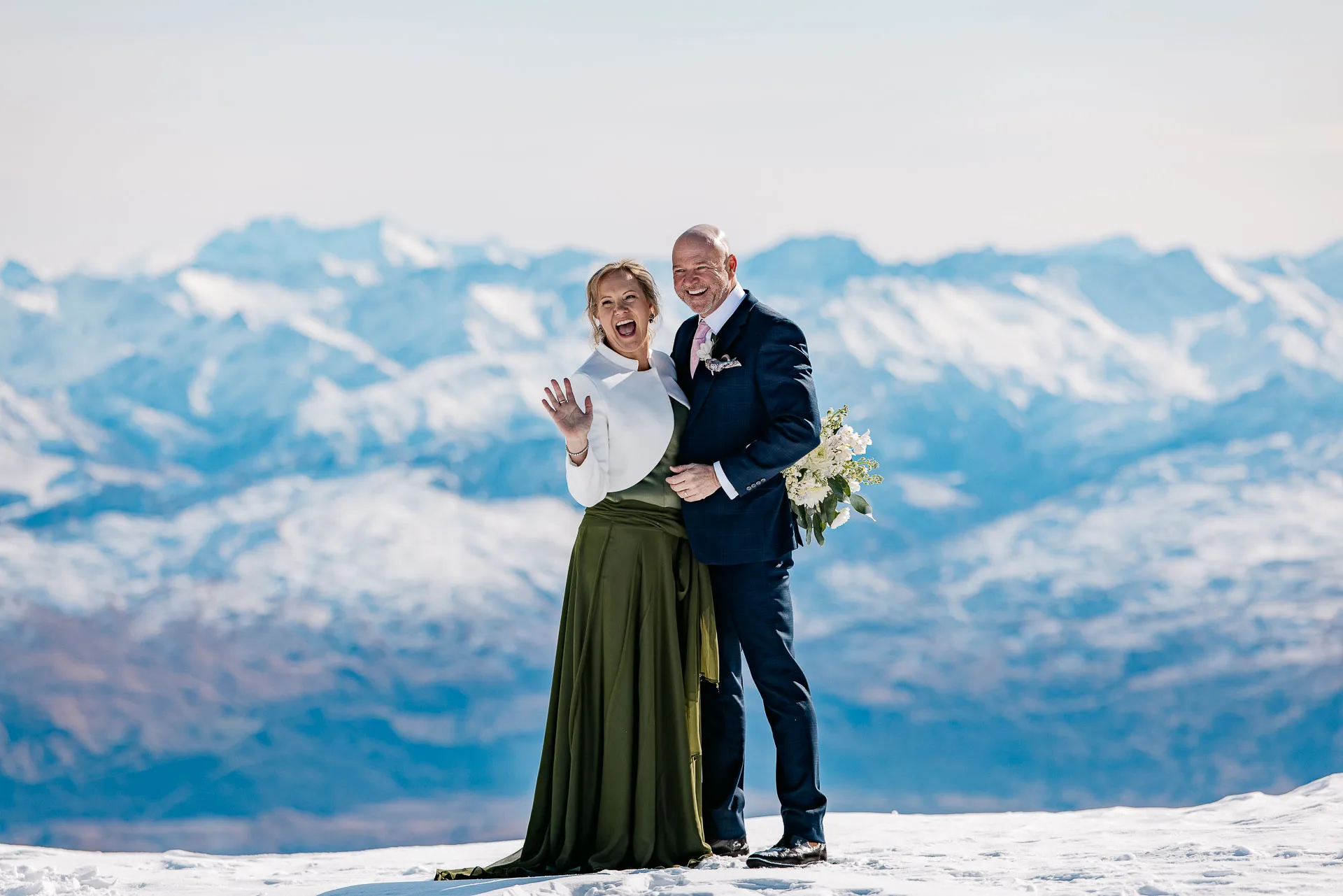 A joyful bride and groom on The Remarkables with the snow-capped Southern Alps behind them