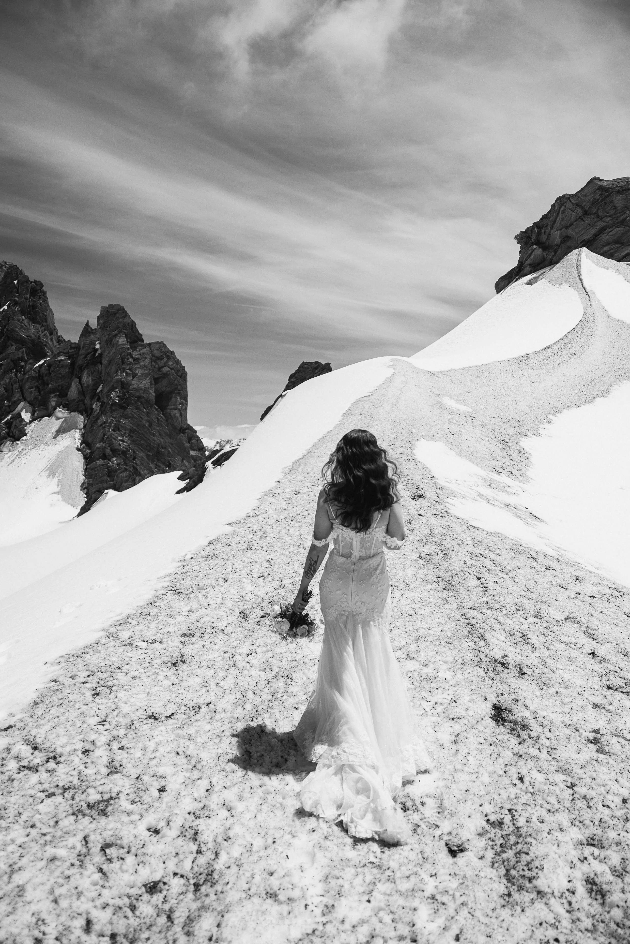 A black-and-white portrait of a bride walking across the snow on Tyndall Glacier