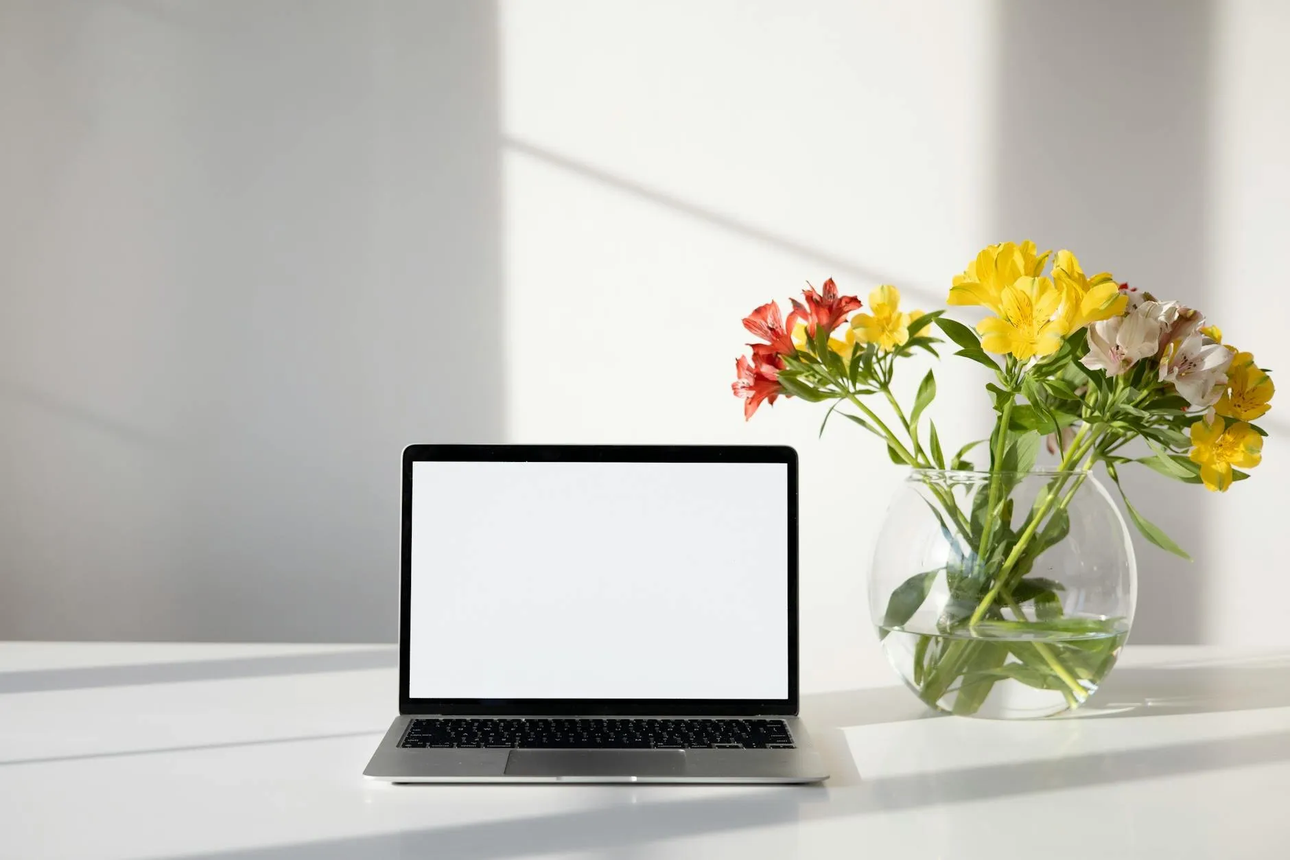 Open laptop beside a vase of bright flowers on a white desk