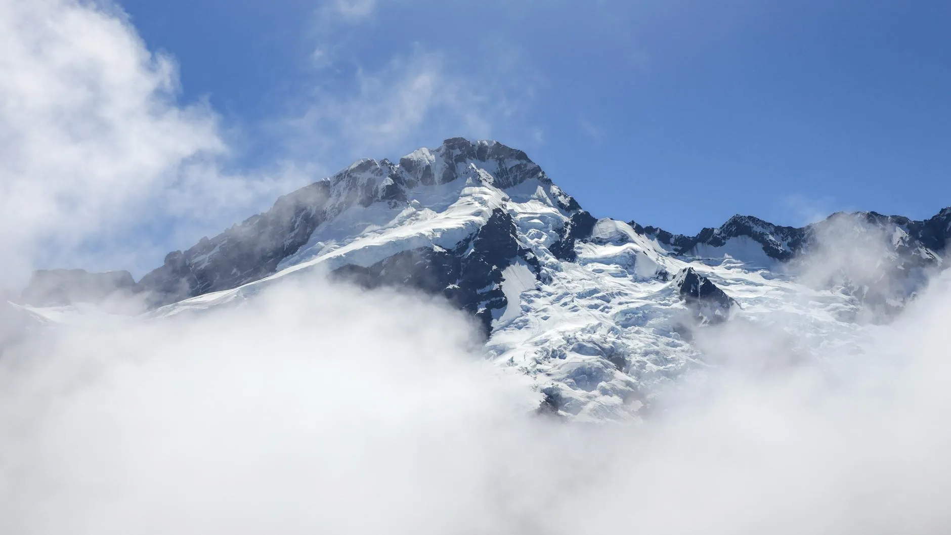 Snow-covered mountain peak rising through cloud
